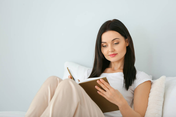 Όμορφη νεαρή γυναίκα διαβάζει βιβλίο στην κρεβατοκάμαρα - Φωτογραφία, εικόνα