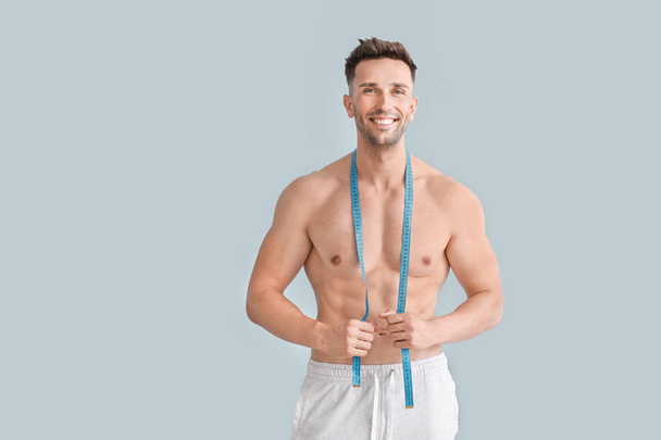 schöner muskulöser Mann mit Maßband auf farbigem Hintergrund. Gewichtsverlust-Konzept - Foto, Bild