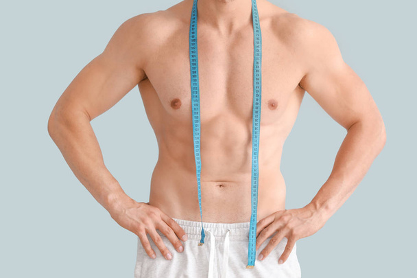 schöner muskulöser Mann mit Maßband auf farbigem Hintergrund. Gewichtsverlust-Konzept - Foto, Bild