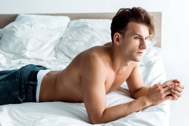 sexy young man in blue jeans lying on bed at home  - Фото, изображение