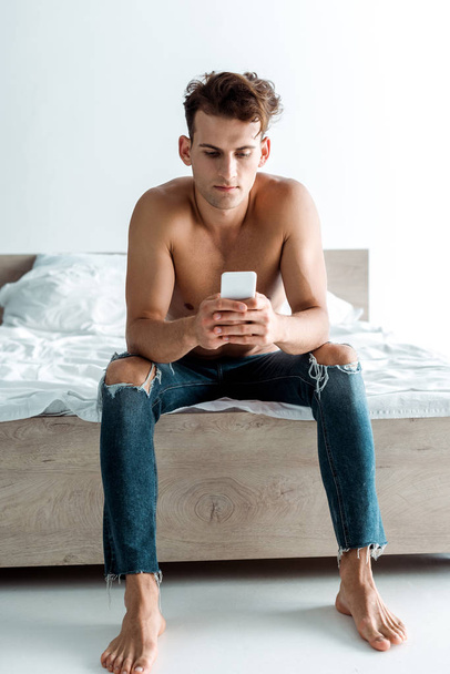 bel homme en jeans en utilisant smartphone dans la chambre
  - Photo, image