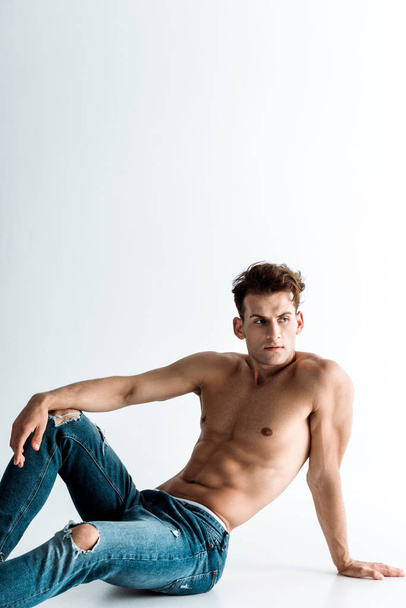 sexy young man in blue denim jeans sitting on white  - Photo, Image