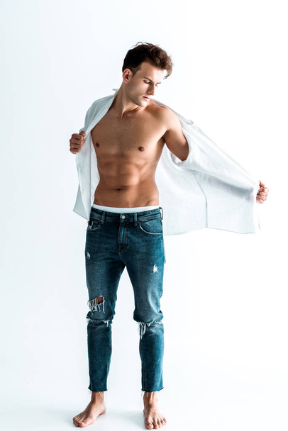 handsome man standing in blue jeans and undressing on white  - Foto, Bild