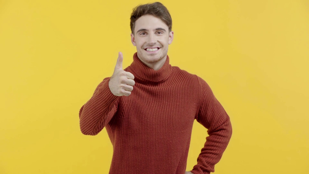 happy man in sweater showing thumb up isolated on yellow - Video