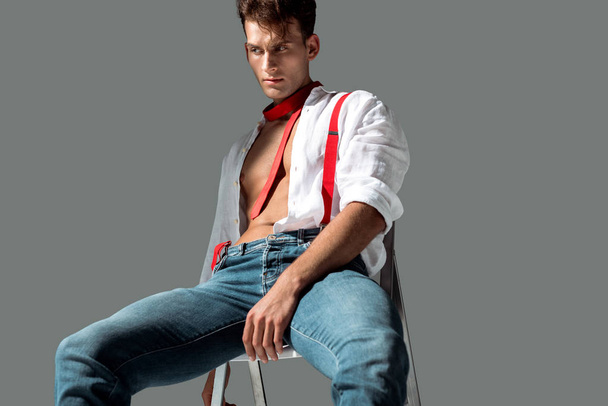 hot young man in white shirt sitting on chair on grey  - Фото, изображение