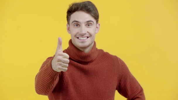 cheerful man in sweater showing thumb up isolated on yellow - Filmati, video