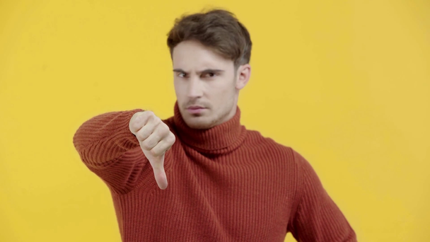 δυσαρεστημένος άντρας με πουλόβερ που δείχνει τον αντίχειρά του απομονωμένο στο κίτρινο - Πλάνα, βίντεο