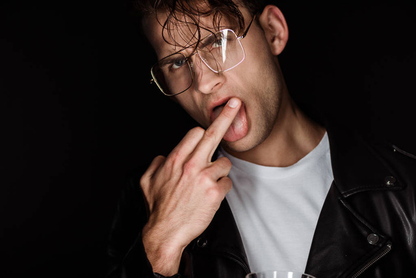 brutal man in glasses showing middle finger while sticking out tongue isolated on black  - Foto, imagen
