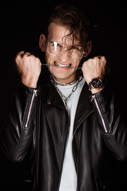 συναισθηματικός άνθρωπος σε γυαλιά δάγκωμα μεταλλικές αλυσίδες απομονώνονται σε μαύρο  - Φωτογραφία, εικόνα