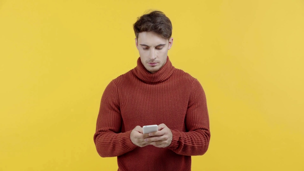 skoncentrowany człowiek w sweter tekstylna na smartphone izolowane na żółtym - Materiał filmowy, wideo