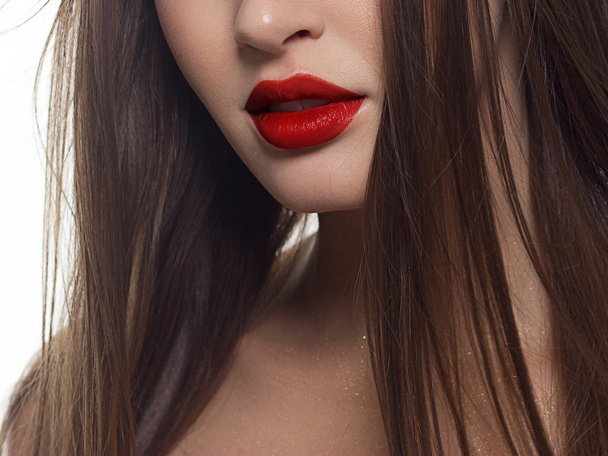 Beauty closeup of women full red lips with shiny skin and long hair. Facial skin care in a spa salon or cosmetology and a fashionable red lip gloss. Evening makeup - Photo, Image