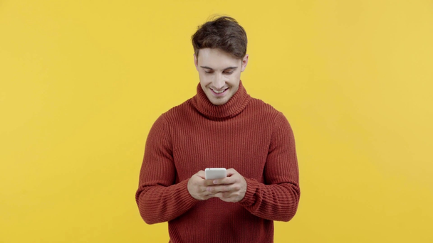 黄色で隔離されたスマートフォン上のセーターのテキストメッセージで幸せな男 - 映像、動画