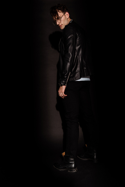 stylish man in glasses and leather jacket standing on black  - Fotoğraf, Görsel