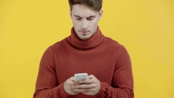 hombre preocupado en suéter mensajes de texto en el teléfono inteligente aislado en amarillo
 - Imágenes, Vídeo