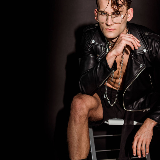 brutal man in leather jacket sitting on black  - Zdjęcie, obraz