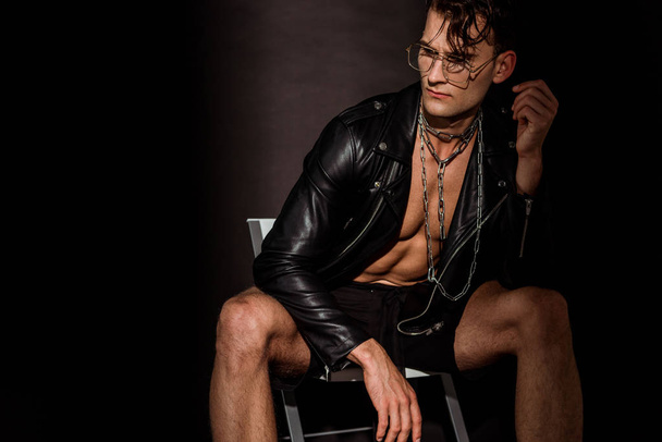 pensive young man in leather jacket sitting on black  - Fotografie, Obrázek
