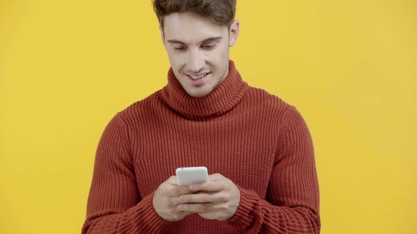 hombre alegre en suéter mensajes de texto en el teléfono inteligente aislado en amarillo
 - Imágenes, Vídeo