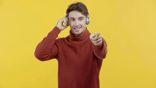Χαμογελώντας άνθρωπος με ακουστικά δείχνοντας με το δάχτυλο απομονώνονται σε κίτρινο - Πλάνα, βίντεο
