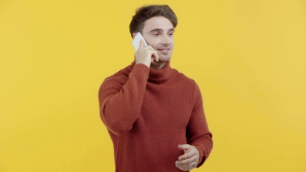 hombre alegre en suéter hablando en teléfono inteligente aislado en amarillo
 - Metraje, vídeo