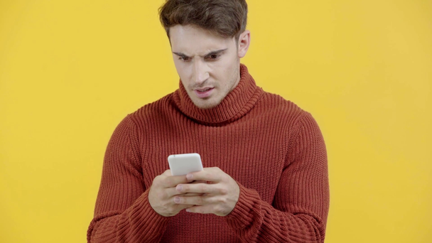 sorprendido hombre en suéter mensajes de texto en el teléfono inteligente aislado en amarillo
 - Imágenes, Vídeo