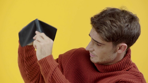 sad man in sweater shaking empty wallet isolated on yellow - Кадри, відео