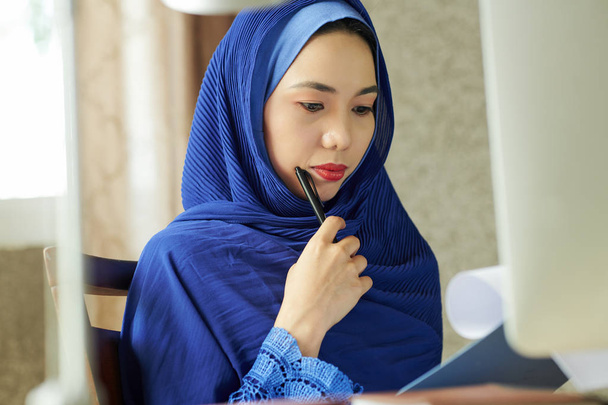 Pensive poważne młode piękne muzułmańskich kobiet w niebieskim dokumencie hidżab czytania i dokonywania korekt - Zdjęcie, obraz