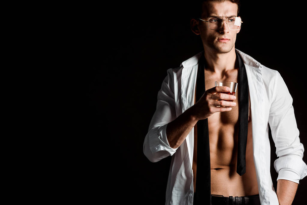 сексуальний бізнесмен в окулярах тримає келих з віскі ізольовані на чорному
  - Фото, зображення
