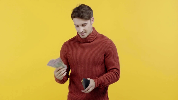 udany mężczyzna w swetrze pokazując pieniądze izolowane na żółto - Materiał filmowy, wideo