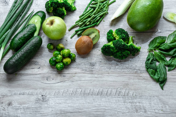 明るいテーブルの上に新鮮な緑の食べ物。アボカドキュウリキャベツリンゴ豆キウイ玉ねぎブロッコリー。健康食品、デトックスベジタリアンの概念。コピースペースフラットレイ. - 写真・画像