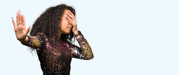 Young beautiful girl with curly hair wearing night party dress covering eyes with hands and doing stop gesture with sad and fear expression. Embarrassed and negative concept. - Фото, зображення