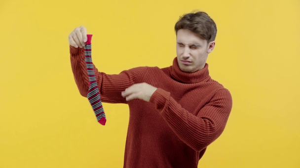 disgusted man in sweater smelling stinky sock isolated on yellow - Footage, Video