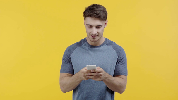 smiling man texting on smartphone isolated on yellow - Кадри, відео