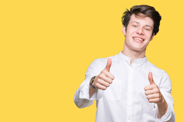 Young handsome business man over isolated background approving doing positive gesture with hand, thumbs up smiling and happy for success. Looking at the camera, winner gesture. - Photo, Image