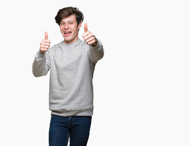 Jóképű sportos fiatalember visel pulóver jóváhagyása során pozitív gesztus kézzel, elszigetelt háttérhez képest remek fel mosolyogva és boldog a siker. Néz a kamerába, győztes gesztus. - Fotó, kép