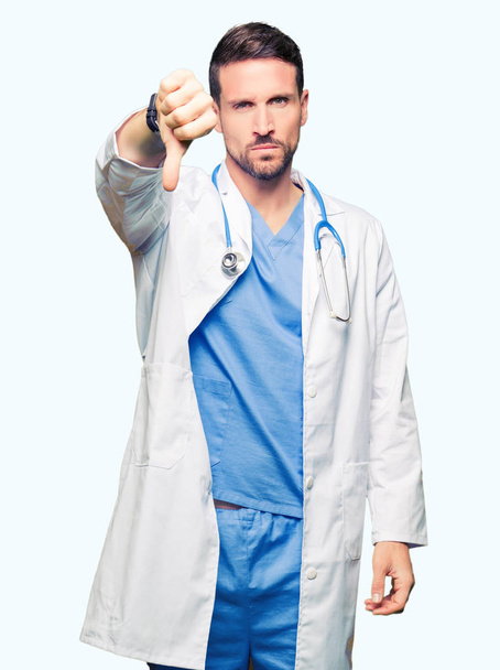 Handsome doctor man wearing medical uniform over isolated background looking unhappy and angry showing rejection and negative with thumbs down gesture. Bad expression. - Foto, Imagem