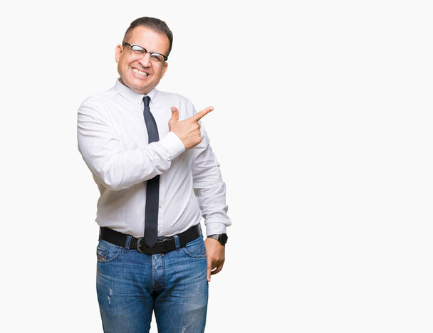 Empresarios de mediana edad árabe hombre con gafas sobre fondo aislado alegre con una sonrisa de la cara señalando con la mano y el dedo hacia arriba a un lado con expresión feliz y natural en la cara
 - Foto, Imagen