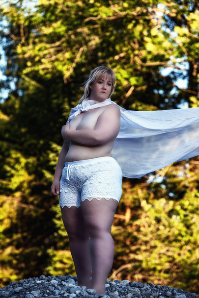 Full-body shot of a in oversize covering her breasts with her arms crossed, wearing a white lace slip and standing in front of a tree in the woods - Photo, Image