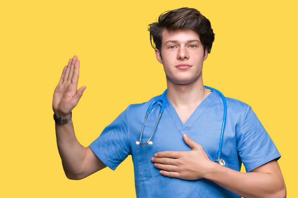 Nuori lääkäri yllään lääketieteellinen univormu yli eristetty tausta Vannoo käsi rinnassa ja avoin kämmen, jolloin uskollisuus lupaus vala
 - Valokuva, kuva