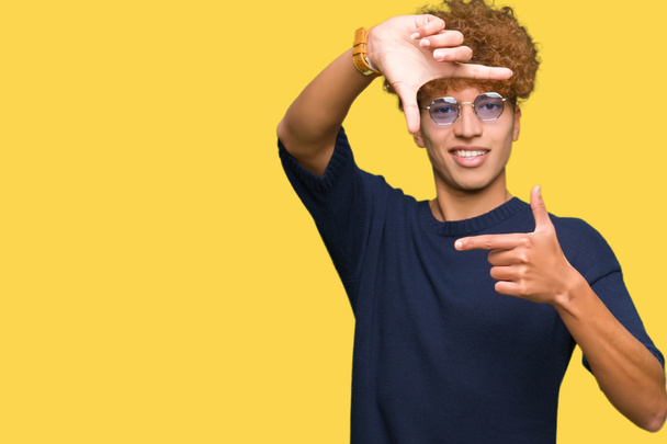 Jóképű fiatalember afro viselt szemüveg Mosolygó döntéshozatali keret kézzel és ujjal boldog arc. A kreativitás és a fotográfia fogalmát. - Fotó, kép