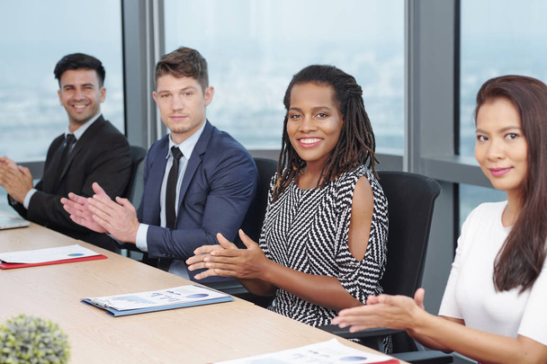 Vrolijke multi-etnische zakenmensen zittend op vergadertafel en applauweding  - Foto, afbeelding