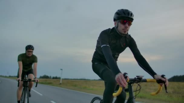 Handsome szakállas profi férfi kerékpáros a verseny kerékpár lovaglás reggel együtt barátnőjével, mindkét viselt védősisakok és a szemüveg, nap, közöttük átszűrődő. - Felvétel, videó