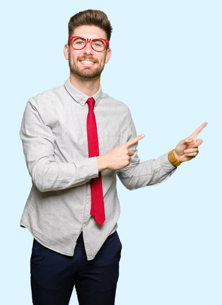 Young handsome business man wearing glasses smiling and looking at the camera pointing with two hands and fingers to the side. - Photo, Image