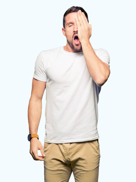 Pohledný muž nosí ležérní bílé tričko Yawning unavený, pokrývá polovinu obličeje, oči a ústa rukou. Tvář bolí bolí. - Fotografie, Obrázek