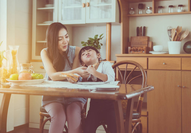 Single mother and little daughter having fun with breakfast together at home kitchen in the morning - 写真・画像