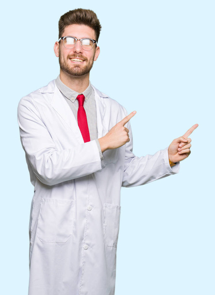 Young handsome scientist man wearing glasses smiling and looking at the camera pointing with two hands and fingers to the side. - Foto, afbeelding