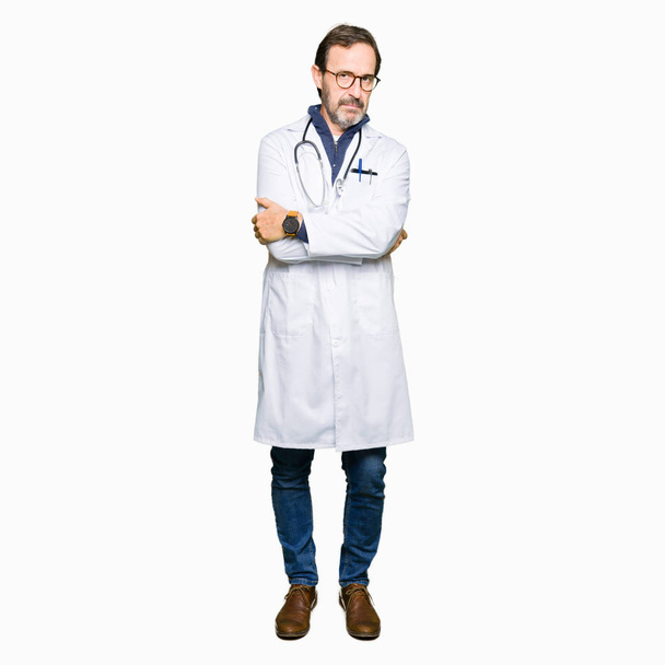 Όμορφος μέση ηλικία γιατρός άνθρωπος φορώντας ιατρική παλτό σκεπτικιστής και νευρικό, αποδοκιμασίας έκφραση προσώπου με σταυρωμένα τα χέρια. Αρνητικό πρόσωπο. - Φωτογραφία, εικόνα