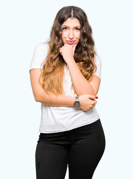 Young beautiful woman wearing casual white t-shirt looking confident at the camera with smile with crossed arms and hand raised on chin. Thinking positive. - Foto, Imagen