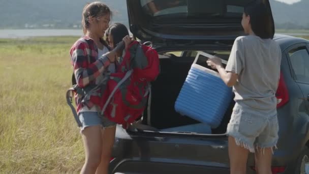 Group of a young teen Asian woman helps to hold backpack and ice cooler with friends camping in nature having a summer traveling. - Footage, Video