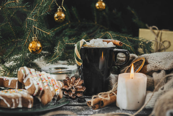 1 mug of hot chocolate with marshmallows and candy, powdered sugar, candle, biscuit, cones, against the background of a knitted sweater and spruce branches with Golden balls, Christmas spirit - Foto, Imagem