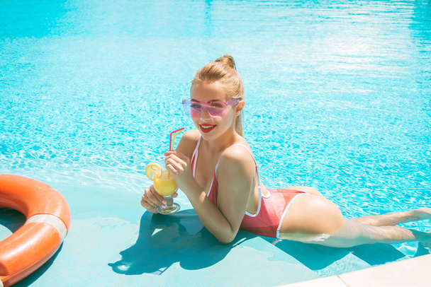 Attractive young girl with a perfect figure in a red bathing suit with a cocktail in the outdoor pool - Фото, зображення